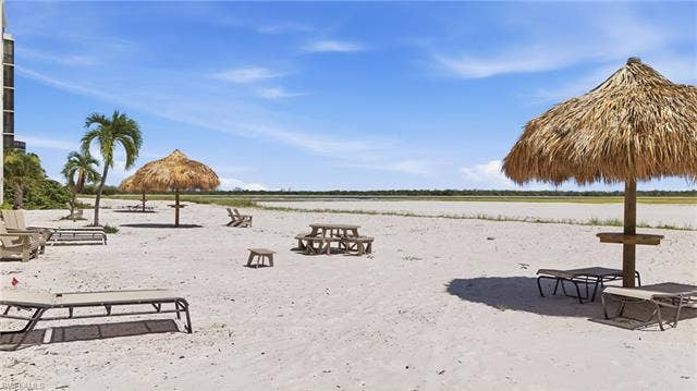 8300 Estero Blvd, #104, Fort Myers Beach, FL 33931 Sandy beach area featuring thatched palapas and palm trees - Virtually Edited Image