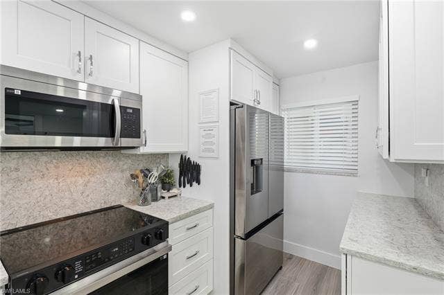8300 Estero Blvd, #104, Fort Myers Beach, FL 33931 White shaker cabinetry, stainless steel appliances, speckled countertops, coordinating backsplash, and wood-finish flooring - Virtually Edited Image