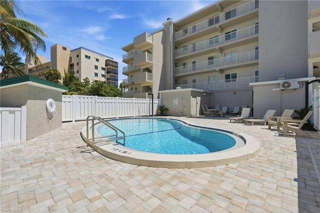 8300 Estero Blvd, #104, Fort Myers Beach, FL 33931 Freeform swimming pool with metal handrails, surrounded by paver decking and a white privacy fence - Virtually Edited Image