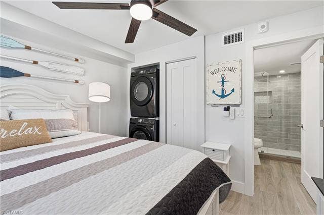 8300 Estero Blvd, #104, Fort Myers Beach, FL 33931 White beadboard headboard, stacked washer and dryer, ceiling fan with integrated lighting, plank-style flooring, and a walk-in shower with tile surround - Virtually Edited Image