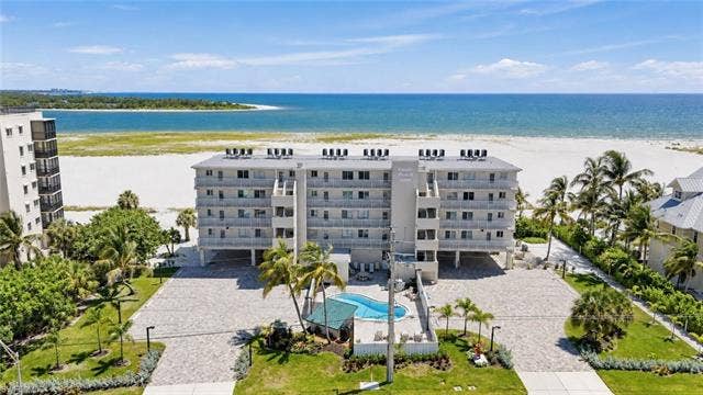 8300 Estero Blvd, #104, Fort Myers Beach, FL 33931 Beachfront condominium building with private balconies, an outdoor swimming pool, and dedicated parking - Virtually Edited Image