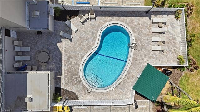 8300 Estero Blvd, #104, Fort Myers Beach, FL 33931 Pebble-finish pool with integrated steps, surrounded by paver patio, and white fencing - Virtually Edited Image