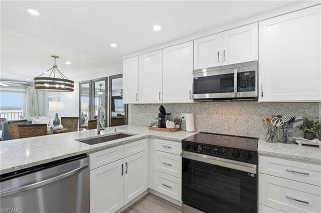 8300 Estero Blvd, #104, Fort Myers Beach, FL 33931 Kitchen featuring white shaker-style cabinetry, stainless steel appliances, light-toned countertops, and a coordinating backsplash - Virtually Edited Image