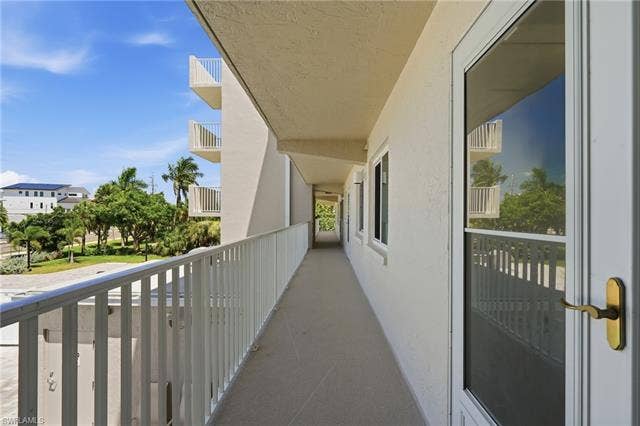 8300 Estero Blvd, #104, Fort Myers Beach, FL 33931 Exterior walkway featuring a metal railing, multiple windows, and an entry door with a brass-finish handle - Virtually Edited Image