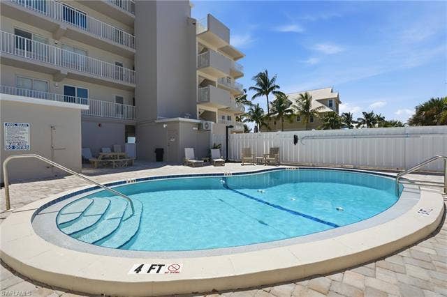 8300 Estero Blvd, #104, Fort Myers Beach, FL 33931 Freeform swimming pool with integrated steps, surrounded by paver patio surfacing, and bordered by a white privacy fence - Virtually Edited Image