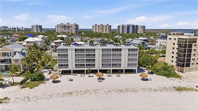 8300 Estero Blvd, #104, Fort Myers Beach, FL 33931 Beachfront building featuring multiple levels of balconies, direct beach access, and surrounding tropical foliage - Virtually Edited Image