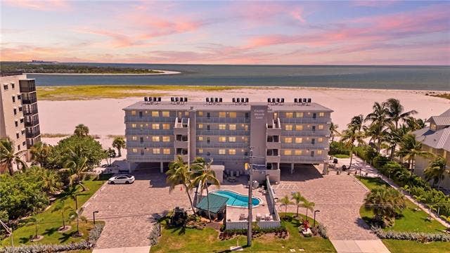 8300 Estero Blvd, #104, Fort Myers Beach, FL 33931 Beachfront condominium building with private balconies, an outdoor swimming pool, and dedicated parking - Virtually Edited Image