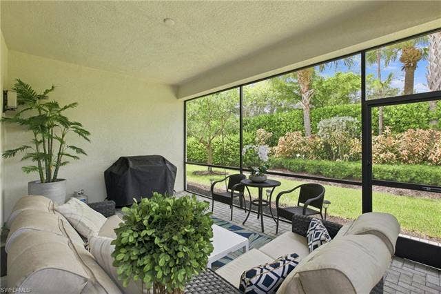 28410 Capraia Dr, Bonita Springs, FL 34135 Screened outdoor living area with a textured ceiling, exterior wall sconce, paver flooring, and landscaped perimeter