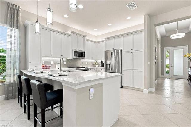 28410 Capraia Dr, Bonita Springs, FL 34135 Kitchen featuring white shaker cabinetry, stainless steel appliances, a white stone countertop island with seating, pendant lighting, and tiled flooring