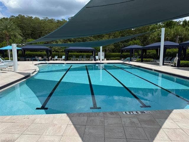 28410 Capraia Dr, Bonita Springs, FL 34135 Lap pool with integrated steps, surrounded by light-toned pavers, and shaded by overhead fabric canopies