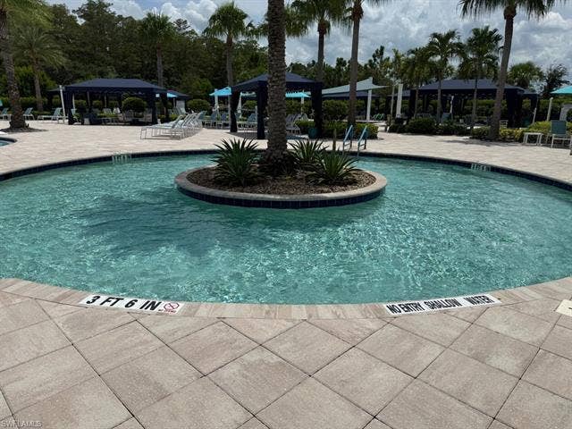 28410 Capraia Dr, Bonita Springs, FL 34135 Resort-style pool area featuring a lazy river design, paver decking, surrounding palm trees, and multiple cabanas
