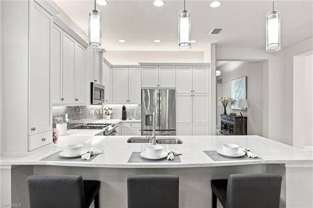 28410 Capraia Dr, Bonita Springs, FL 34135 Kitchen with white shaker-style cabinetry, stainless steel appliances, a tile backsplash, and a large island with an undermount sink