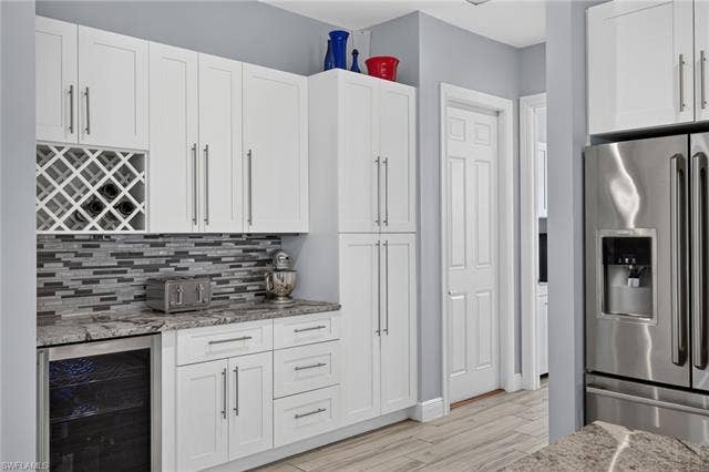 27150 Rue De Paix, Bonita Springs, FL 34135 White cabinetry including pantry cabinet rollouts, integrated wine storage, mosaic tile backsplash, countertop with an under-counter beverage cooler, and a stainless steel refrigerator