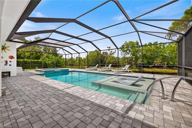 27150 Rue De Paix, Bonita Springs, FL 34135 Screened-in outdoor pool area featuring a rectangular pool, sun shelf, integrated spa, and paver decking