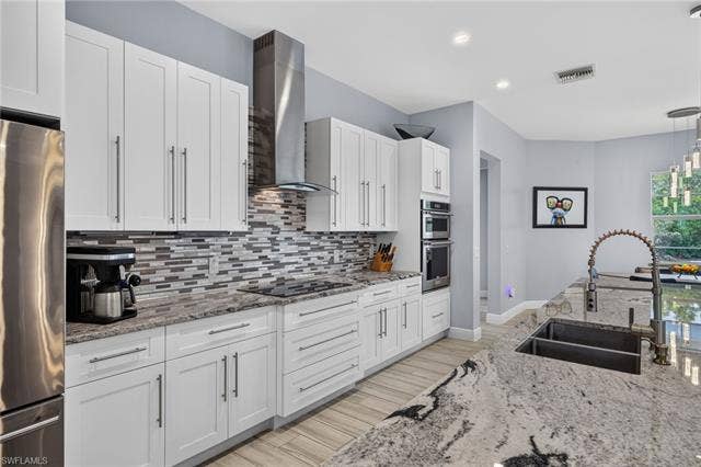 27150 Rue De Paix, Bonita Springs, FL 34135 White cabinetry, stainless steel appliances, stainless range hood, mosaic tile backsplash, double basin sink, and pendant lighting