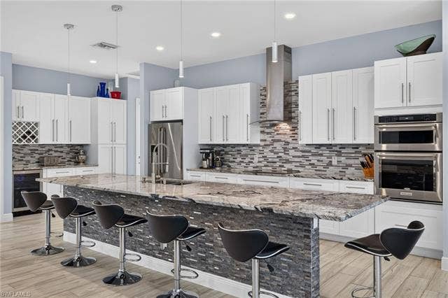27150 Rue De Paix, Bonita Springs, FL 34135 Modern kitchen featuring white cabinetry, stainless steel appliances, a large island with stone finish, beverage fridge and modern lighting