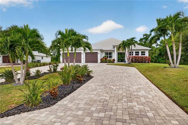 27150 Rue De Paix, Bonita Springs, FL 34135 Modern stucco exterior, paver driveway, mature palm trees, attached three-car garage, and established landscaping