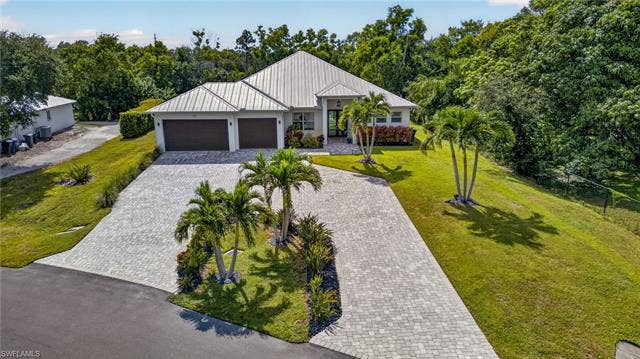 27150 Rue De Paix, Bonita Springs, FL 34135 Large circular paver driveway, three-car garage, lush landscaping, and mature palm trees
