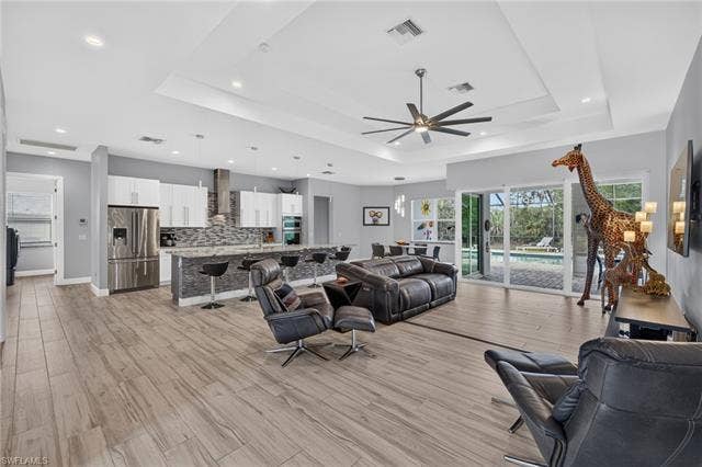 27150 Rue De Paix, Bonita Springs, FL 34135 Open concept living area featuring plank tile flooring, a tray ceiling with recessed lighting, and a kitchen with white cabinetry and stainless steel appliances