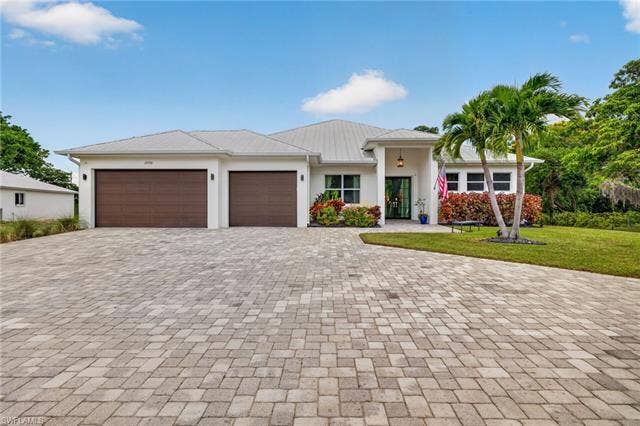 27150 Rue De Paix, Bonita Springs, FL 34135 White exterior with a metal roof, two distinct garage doors, and a paver driveway