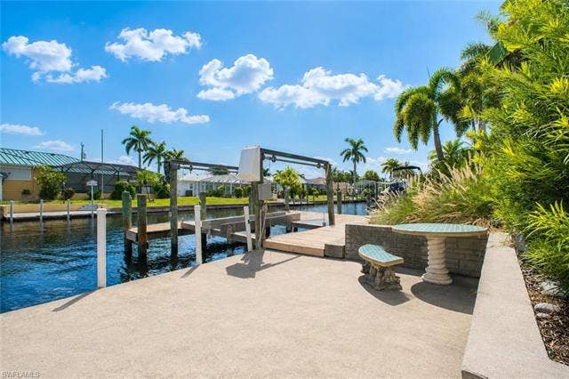 5219 S Seminole Ct, Cape Coral, FL 33904 Concrete patio with built-in planter, lush landscaping, and a waterfront boat dock featuring a boat lift