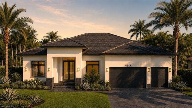 5219 S Seminole Ct, Cape Coral, FL 33904 (Rendered photo) Modern stucco facade with a dark tile roof, paved driveway, two garage doors, and front entry with double glass doors