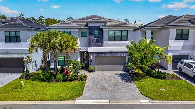 20390 Fair Oak Ln, Estero, FL 33928 Modern stucco exterior with dark tile roofing, a paver driveway, and an integrated garage