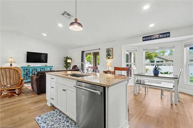 4618 Sierra Ln, Bonita Springs, FL 34134 Open-concept living area with wood-finish flooring, white cabinetry, a kitchen island with a built-in sink, and a bay window