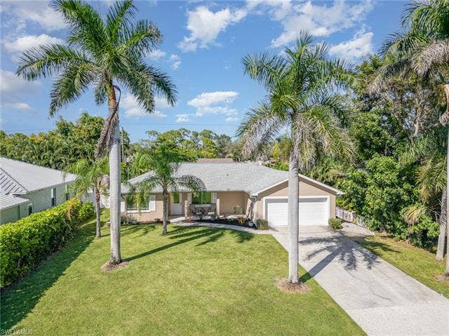 4618 Sierra Ln, Bonita Springs, FL 34134 Single-story residence with a two-car garage, concrete driveway, and mature palm trees