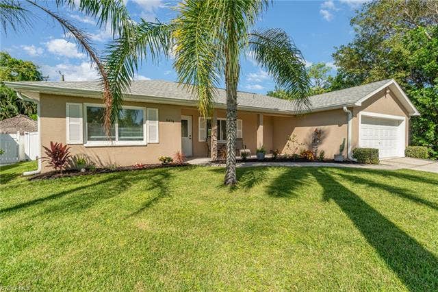 4618 Sierra Ln, Bonita Springs, FL 34134 Stucco exterior with white shutters, an attached garage, and landscaping with mature trees