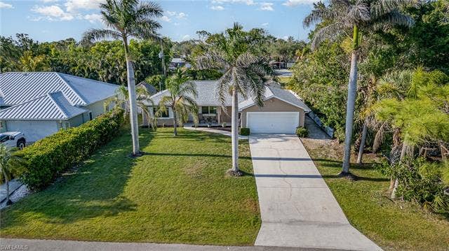 4618 Sierra Ln, Bonita Springs, FL 34134 Well-maintained lawn, mature palm trees, concrete driveway, attached garage, and stucco exterior
