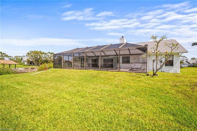 20640 Porthole Ct, Estero, FL 33928 Rear view of property featuring glass enclosure, a yard, a patio area, and a chimney