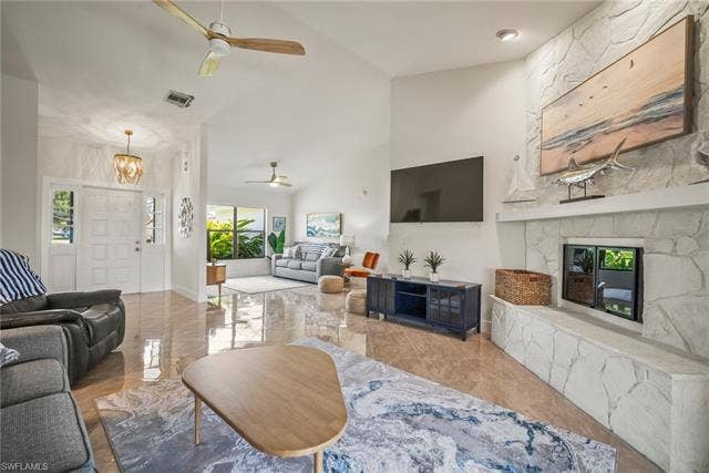 20640 Porthole Ct, Estero, FL 33928 Living room with marble finish floor, visible vents, a fireplace, high vaulted ceiling, and ceiling fan with notable chandelier