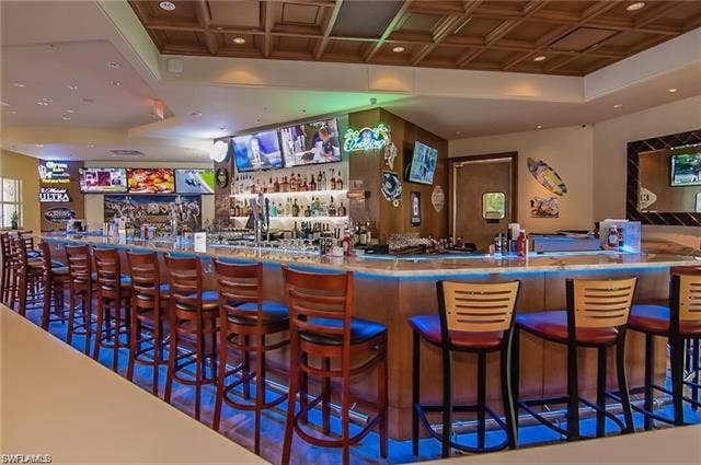 15059 Blue Marlin Ter, Bonita Springs, FL 34135 Expansive bar area featuring a wood-finish counter with integrated lighting, multiple television screens, and a coffered ceiling offervhapoy hr daily