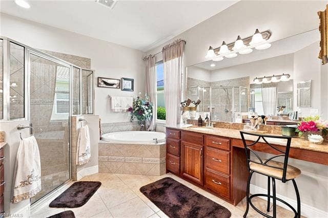 19600 Maddelena Cir, Estero, FL 33967 Walk-in shower with clear glass enclosure, built-in soaking tub, wood-finish vanity with ample storage, large vanity mirror, and tile flooring