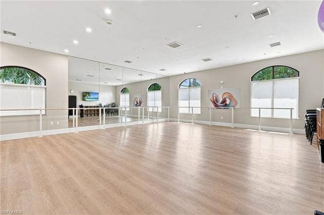 19600 Maddelena Cir, Estero, FL 33967 Spacious room featuring wood-finish flooring, full-wall mirrors, integrated ballet barres, recessed lighting, and arched windows with roller shades