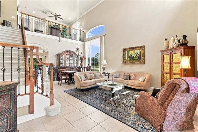 19600 Maddelena Cir, Estero, FL 33967 Two-story living area featuring high ceilings, a grand staircase with wrought iron balusters, tile flooring, and large windows with arched transoms