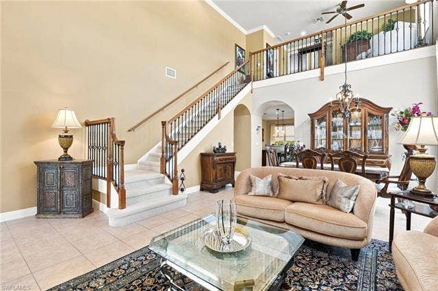 19600 Maddelena Cir, Estero, FL 33967 Two-story living area with high ceilings, tile flooring, and a grand staircase with wood newel posts and wrought iron balusters