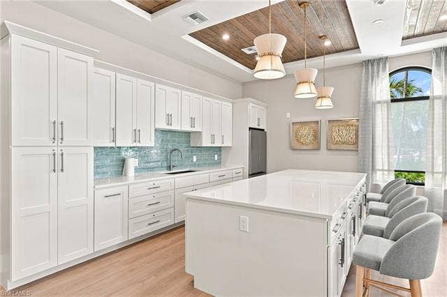 19600 Maddelena Cir, Estero, FL 33967 White shaker cabinetry, light wood-finish flooring, wood plank ceiling accent, large kitchen island with integrated seating, and a tiled backsplash