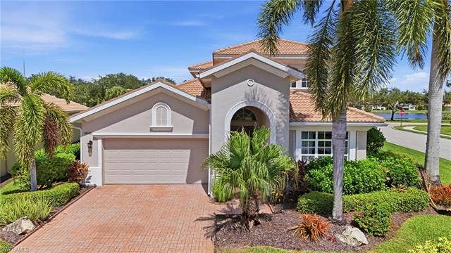 19600 Maddelena Cir, Estero, FL 33967 Stucco exterior with a tile roof, arched entry, paver driveway, and an integrated garage