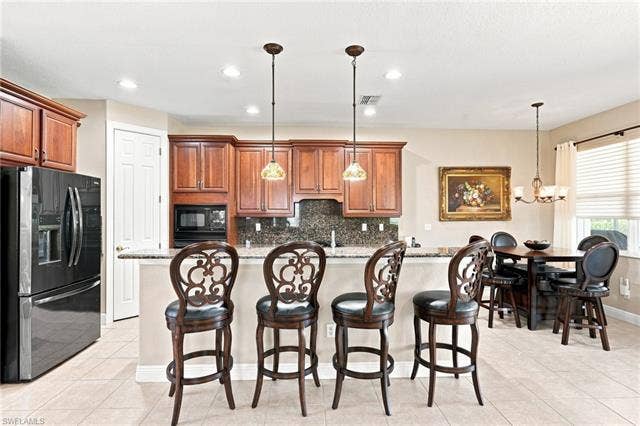 19600 Maddelena Cir, Estero, FL 33967 Kitchen featuring wood cabinetry, integrated microwave, pendant lighting, and a breakfast bar with stone countertops