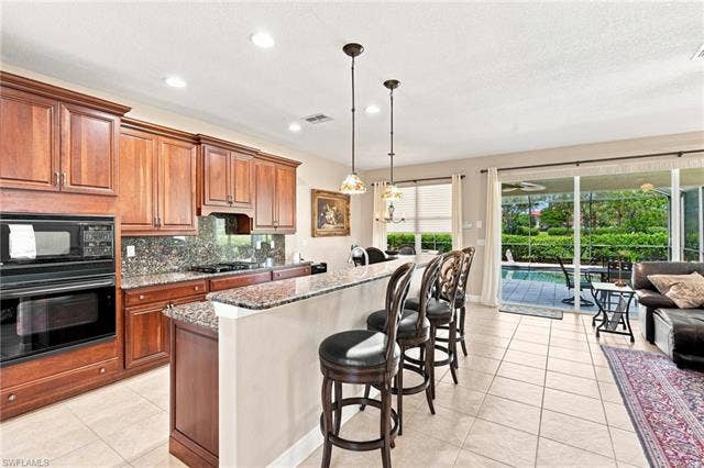 19600 Maddelena Cir, Estero, FL 33967 Kitchen featuring wood cabinetry, built-in wall oven and microwave, granite countertops, and tile flooring