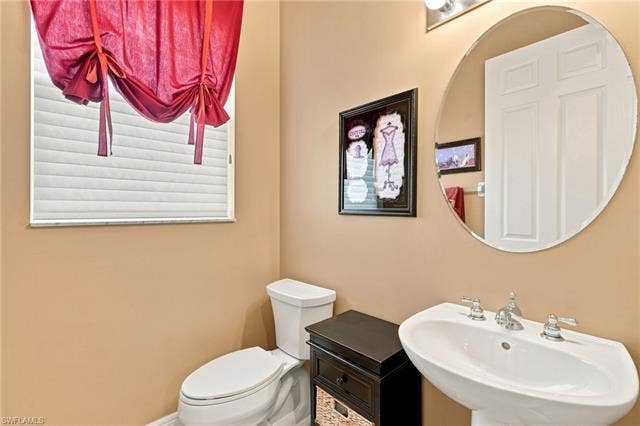 19600 Maddelena Cir, Estero, FL 33967 Pedestal sink with chrome fixtures, oval mirror, and a window with blinds