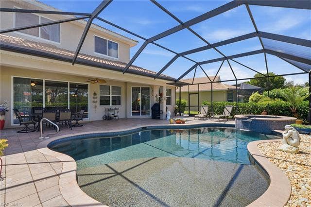 19600 Maddelena Cir, Estero, FL 33967 Screened-in pool deck featuring a freeform swimming pool, integrated spa with waterfall, and a tiled patio