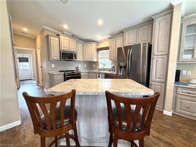 4710 W Lafayette Ln, Estero, FL 33928 Kitchen featuring wood-finish flooring, an island with seating, stainless steel appliances, light-toned cabinetry, and a tile backsplash