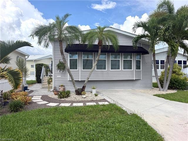 4710 W Lafayette Ln, Estero, FL 33928 Siding exterior with multiple windows, a front awning, mature palm trees, and a paved driveway