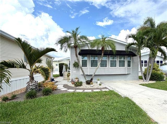 4710 W Lafayette Ln, Estero, FL 33928 Exterior featuring light gray siding, multiple palm trees, a well-maintained lawn, a concrete driveway, and a decorative stone pathway