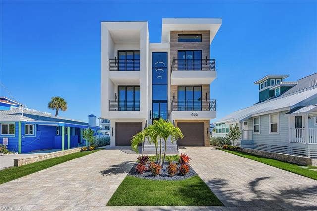 455 Palermo Cir, Fort Myers Beach, FL 33931 Contemporary house featuring stucco siding, decorative driveway, an attached garage, and a balcony - Virtually Edited Image