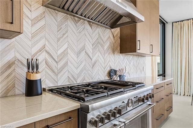 455 Palermo Cir, Fort Myers Beach, FL 33931 Kitchen featuring custom exhaust hood, range with two ovens, light stone countertops, modern cabinets, and tasteful backsplash - Virtually Edited Image