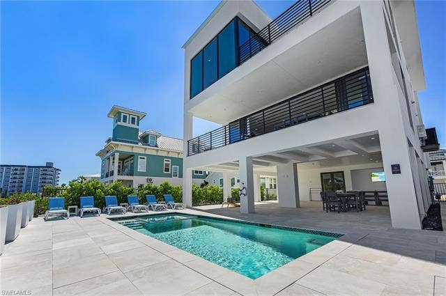 455 Palermo Cir, Fort Myers Beach, FL 33931 Rear view of house with a patio, a balcony, a pool with connected hot tub, and stucco siding - Virtually Edited Image